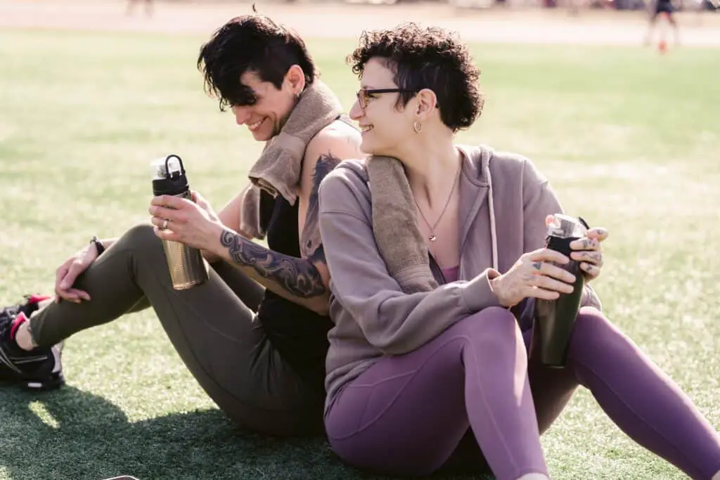 Two persons wearing leggings sitting down and holding water bottles