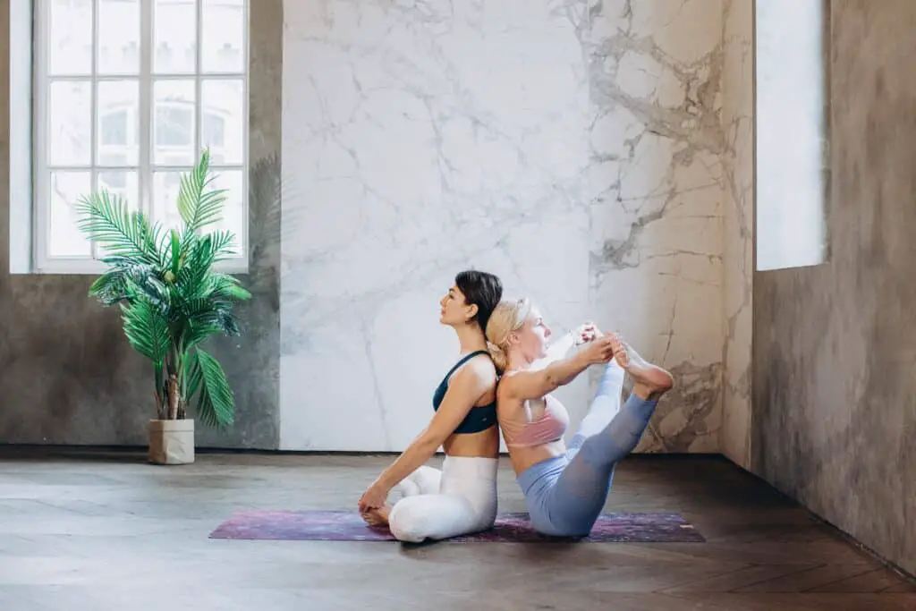 two women stretching back to back wearing a white and light blue see though leggings