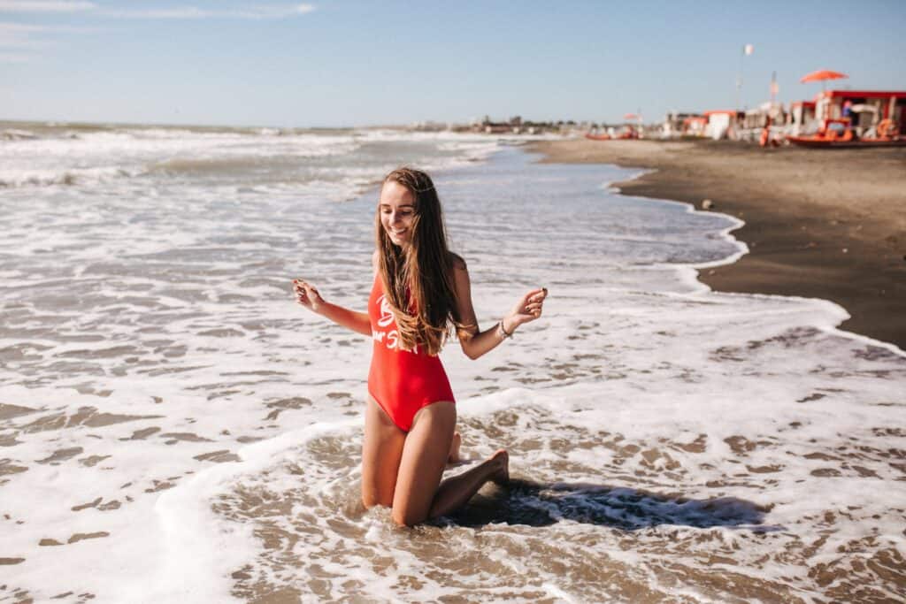 A woman in a red suit kneeling on the beach