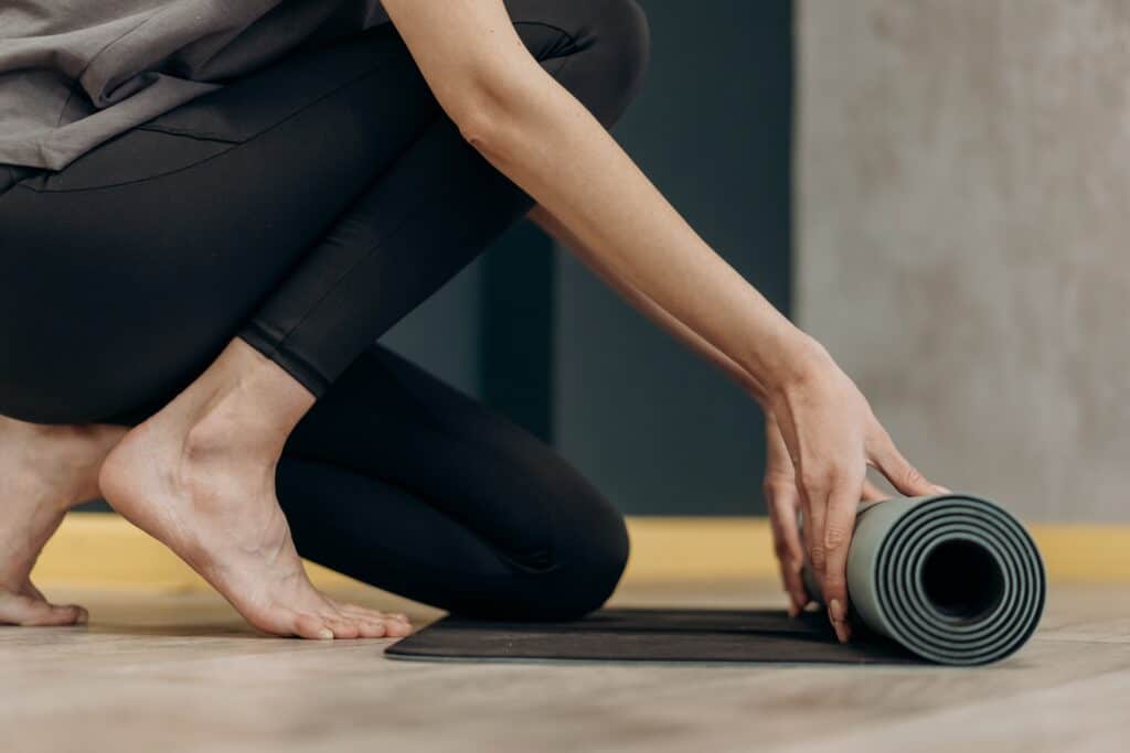 a woman wearing black yoga pants rolling a yoga mat