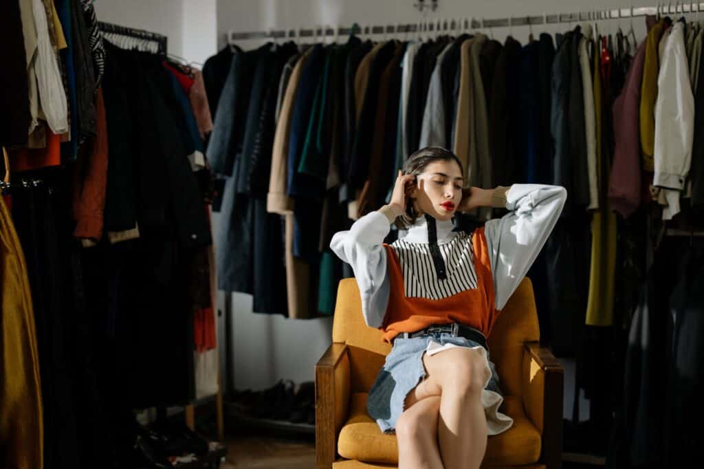 A woman sitting on a chair with hanged clothes at the background