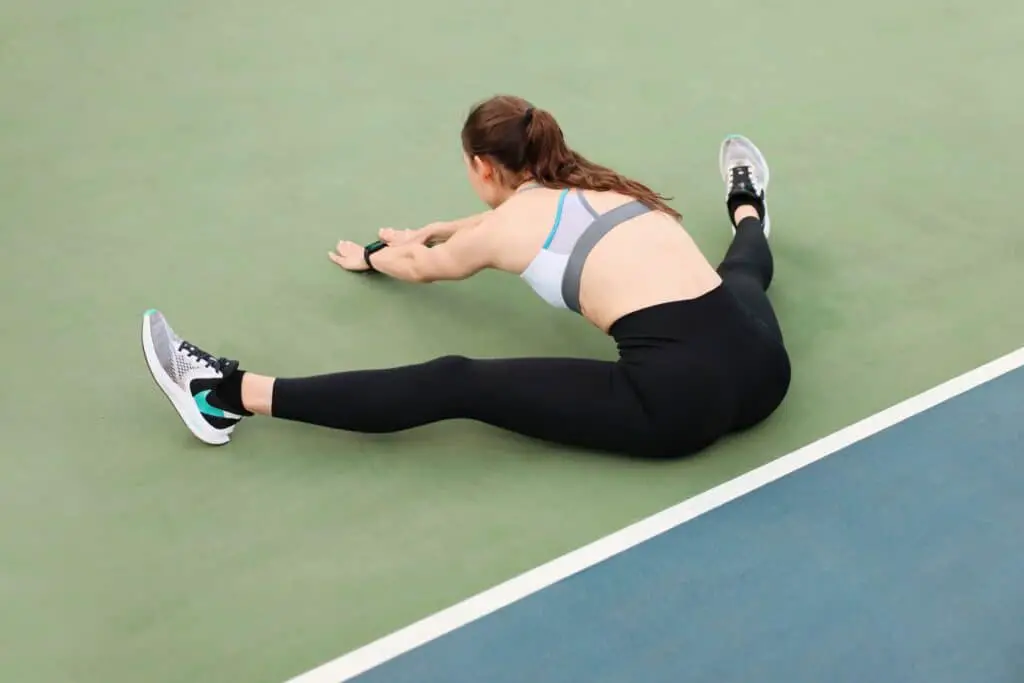 A woman stretching on a green floor while wearing leggings