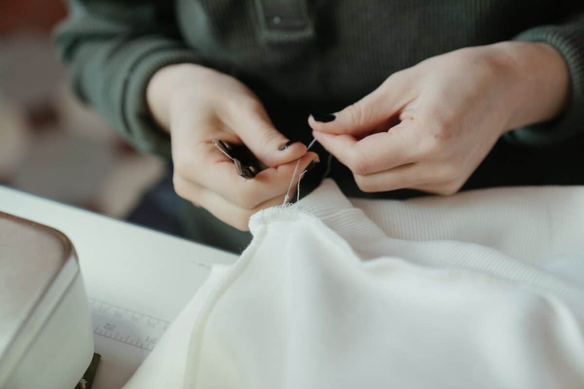 A woman with black nail polish removes a white thread on a white piece of clothing on a table