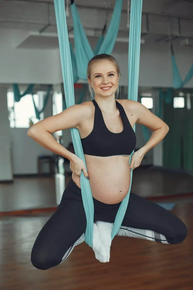 A pregnant woman wearing a black sports bra and black leggings doing aerial balance yoga in the gym