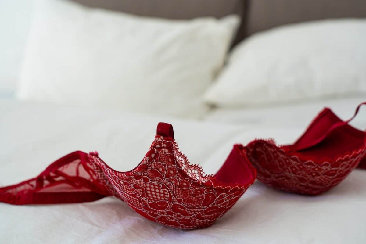 Red lace bra near a white pillow placed on top of a white bedsheet