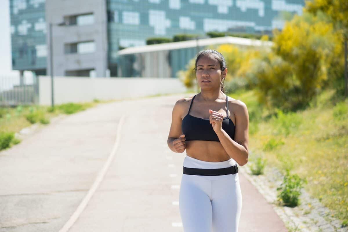 A woman with black hair wears a black sports bra and white leggings on an empty street