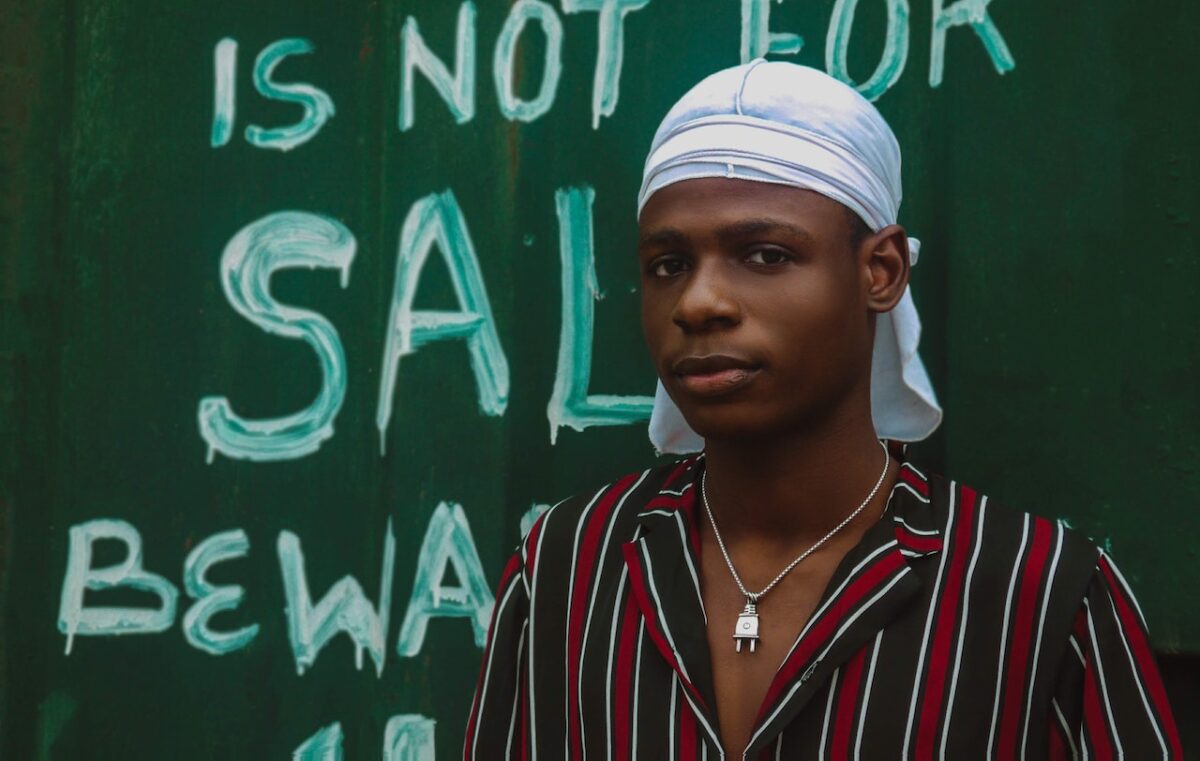 A man wearing a striped shirt and white wave cap is standing on a green wall