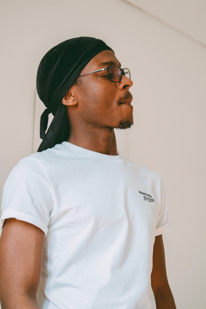 A man in a white crew neck t-shirt and black durag standing near a white wall