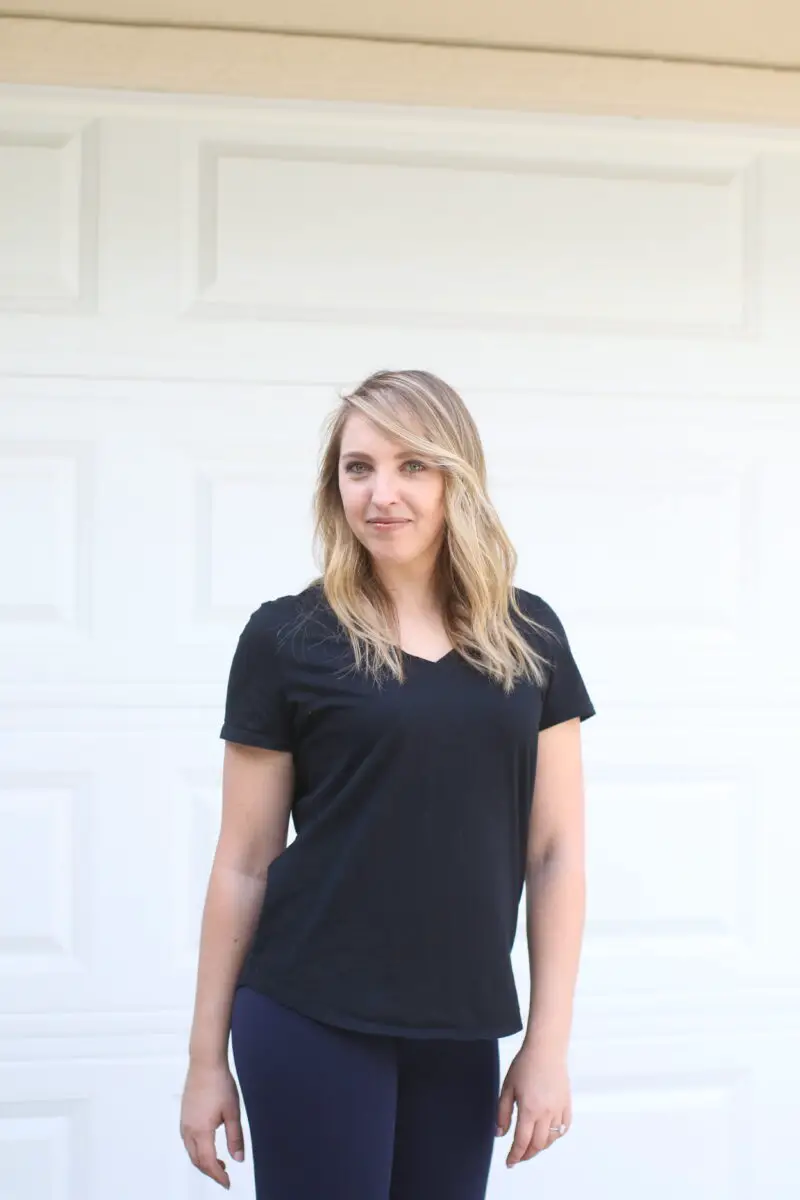 Woman in a black t-shirt and blue leggings standing near a white wall