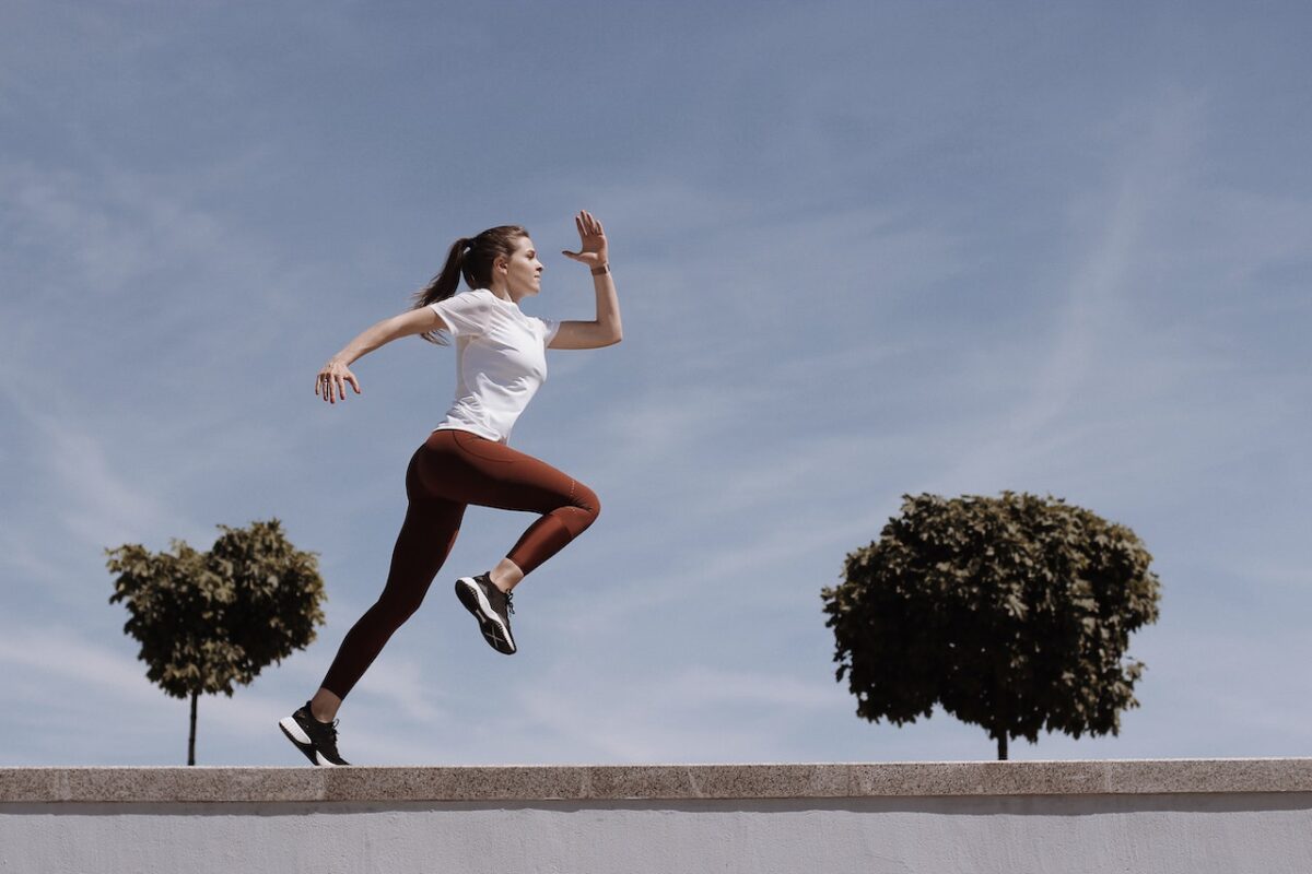 A woman in a white t-shirt and brown leggings wearing black rubber shoes running in the park