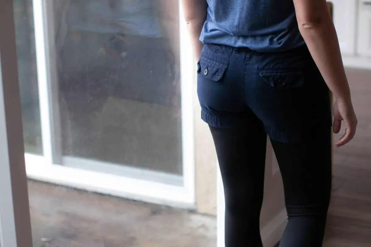 A person wearing blue shorts over black leggings standing near a window in the living room