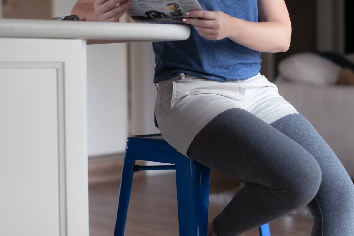 A person wearing beige shorts over gray leggings sitting on a blue chair in the living room