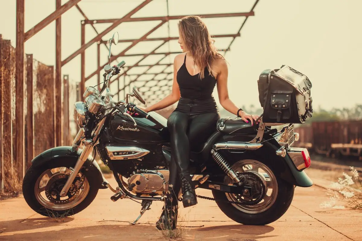 Woman in a black tan top and black leggings wearing black boots sitting on a big motorbike.