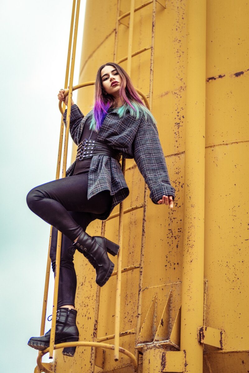 Woman in a checked long-sleeves and black leggings wearing black boots standing on a steel ladder