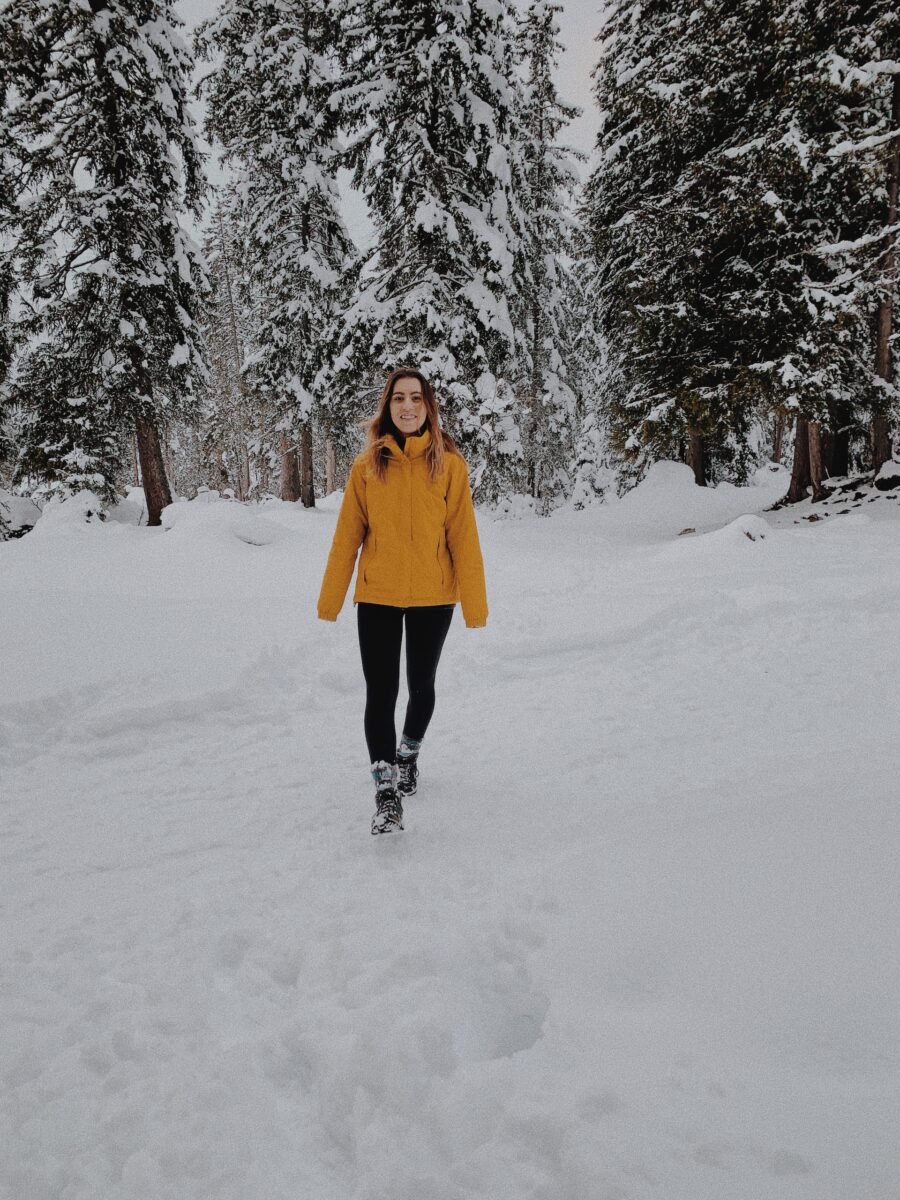 Woman in a yellow jacket and black leggings wearing black boots standing in the middle of a snowy park