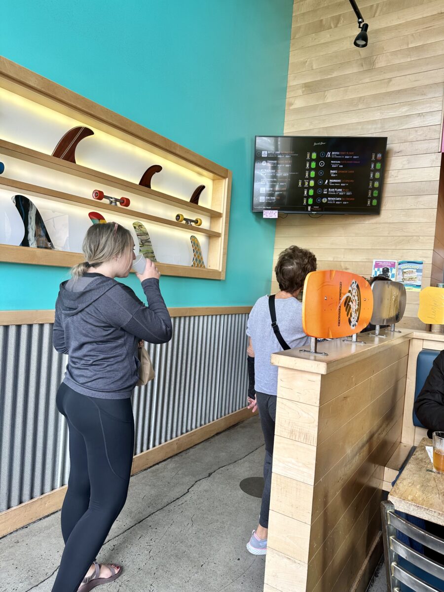 Woman in a gray jacket and black yoga pants drinking water while waiting in line at a fast food