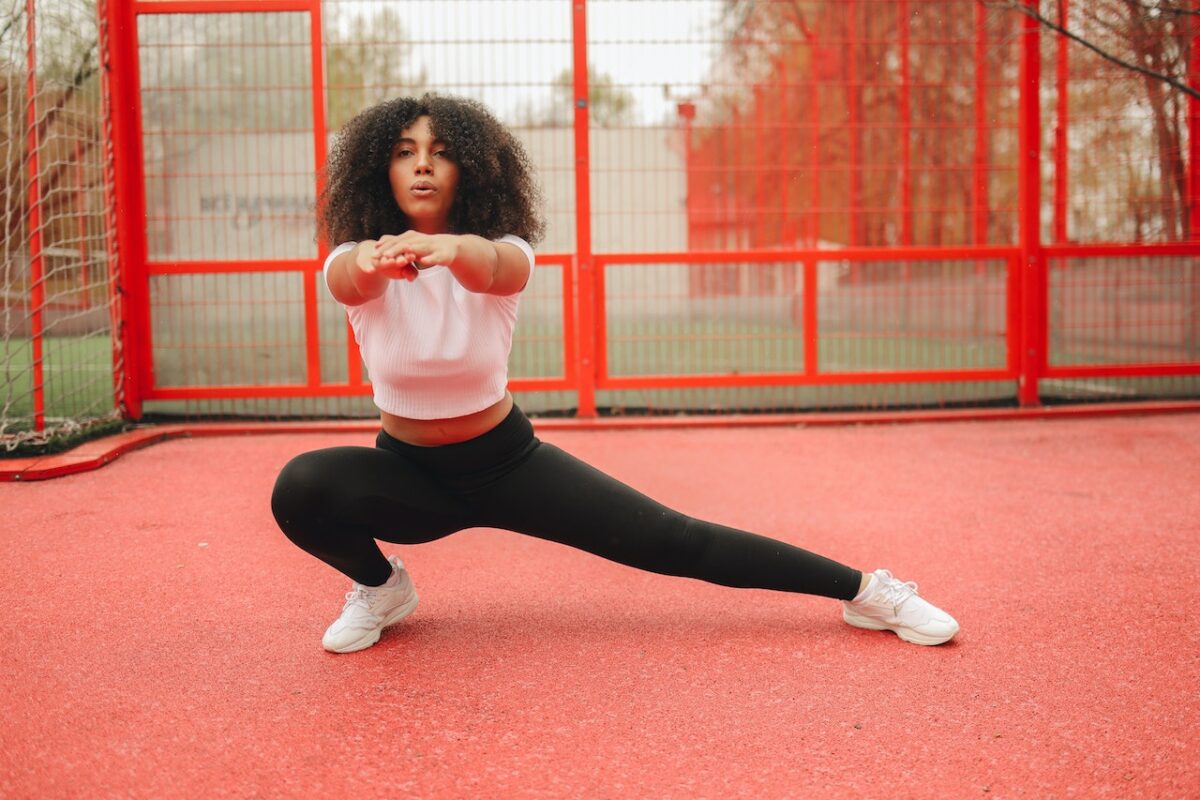 A woman in a white short t-shirt and black leggings wearing white rubber shoes working out in the park