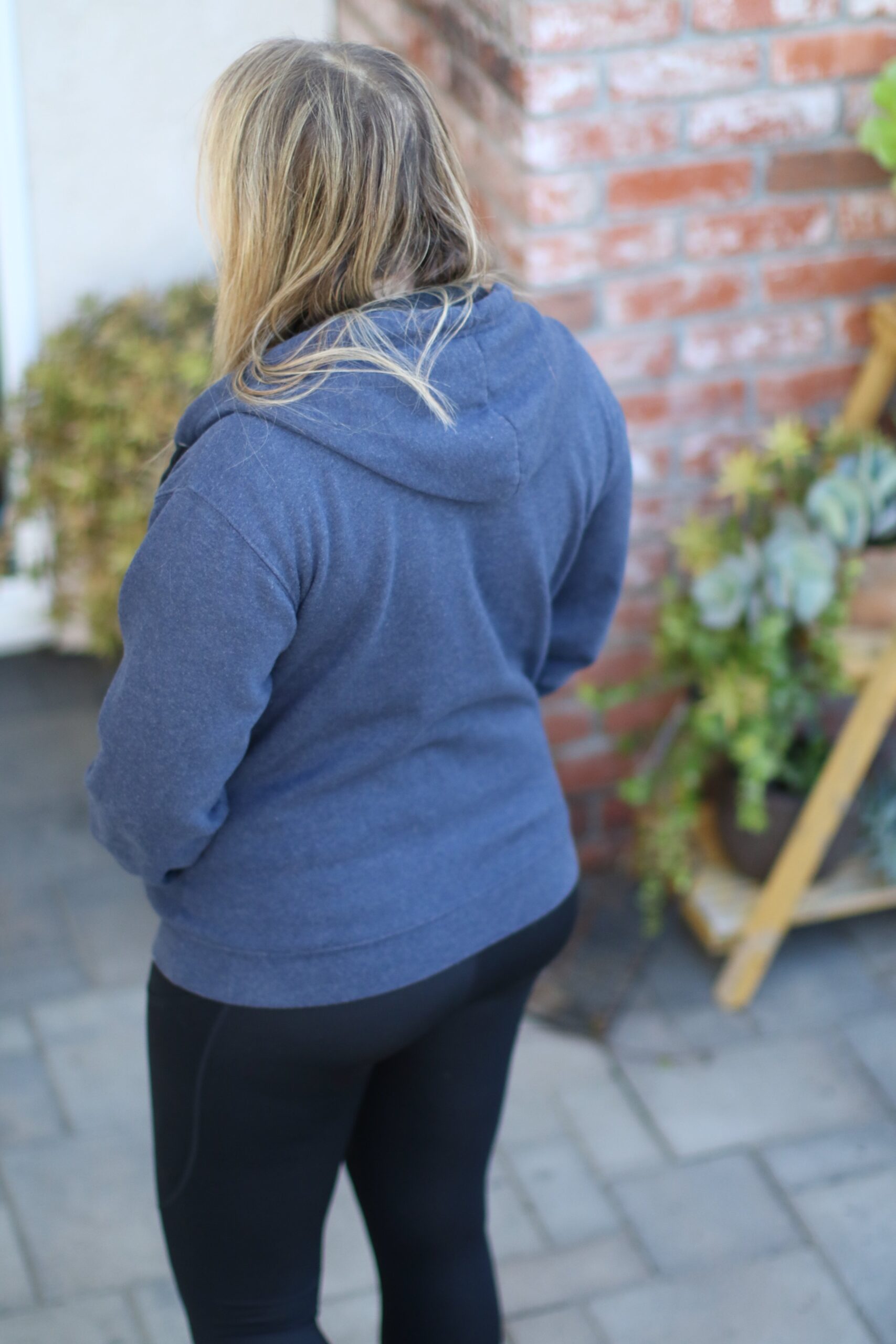 Woman wearing a blue hoodie with black spandex leggings outside on a patio