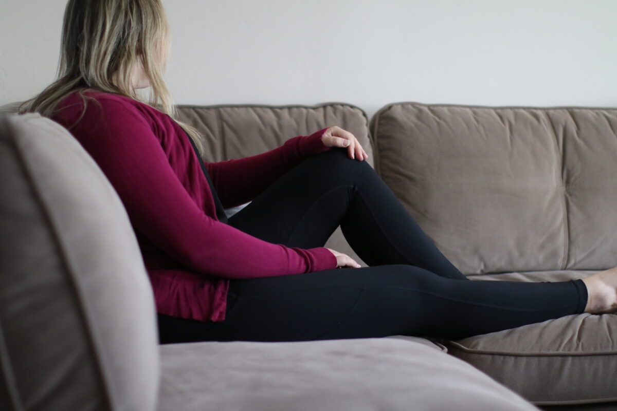 Woman lounging on a gray couch in the living room while wearing black leggings and a pink cardigan