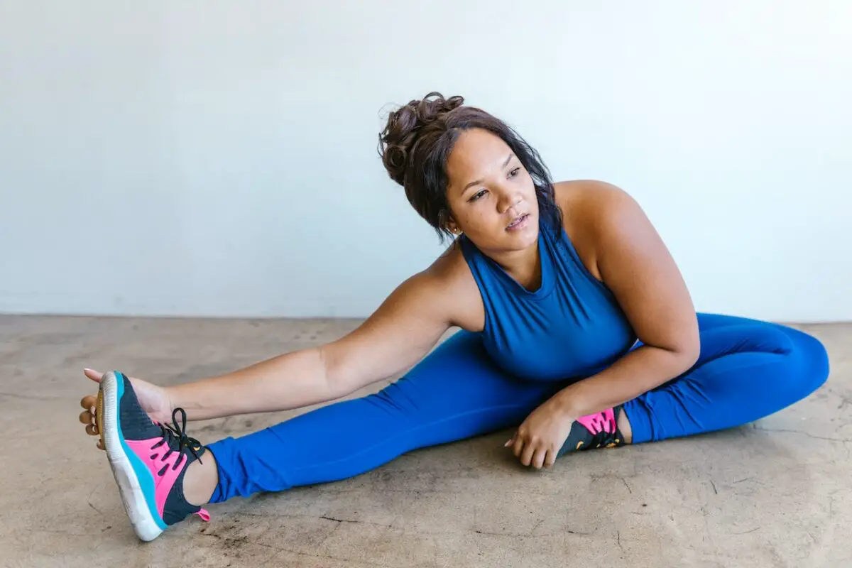 A woman wearing a blue sleeveless top and blue leggings doing a stretching