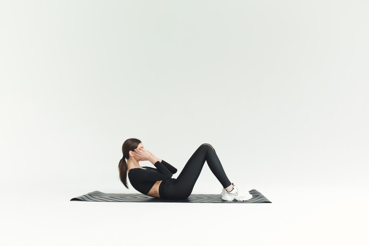 A woman wearing a black long-sleeved crop top and black leggings doing a sit-up
