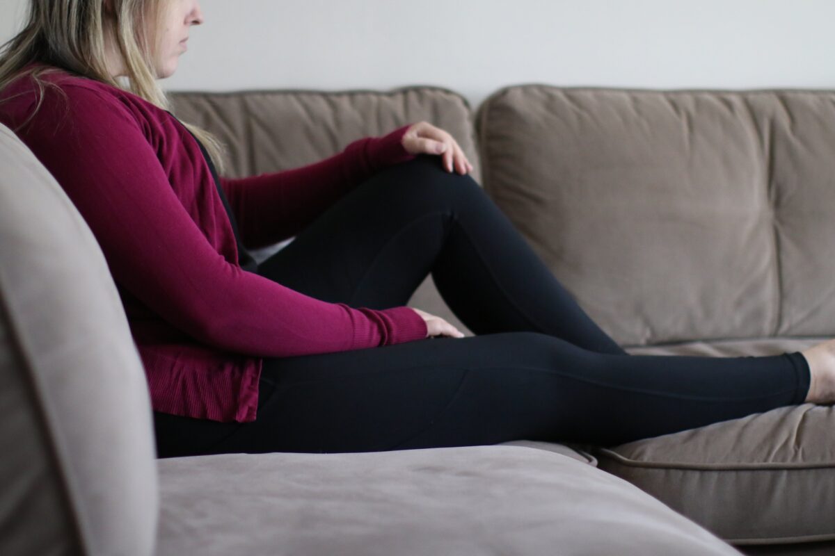 Woman relaxing on a gray couch in the living room while wearing a magenta sweater and black leggings