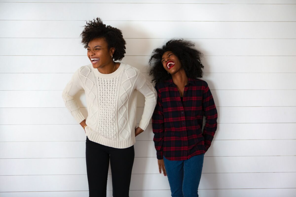 A woman wearing a white knitted sweatshirt and black leggings while the other woman is wearing a checkered long-sleeve and pants