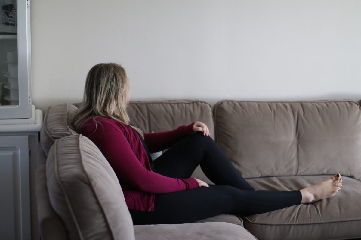 Woman wearing a dark pink cardigan and black spandex leggings sitting on a gray couch in the living room