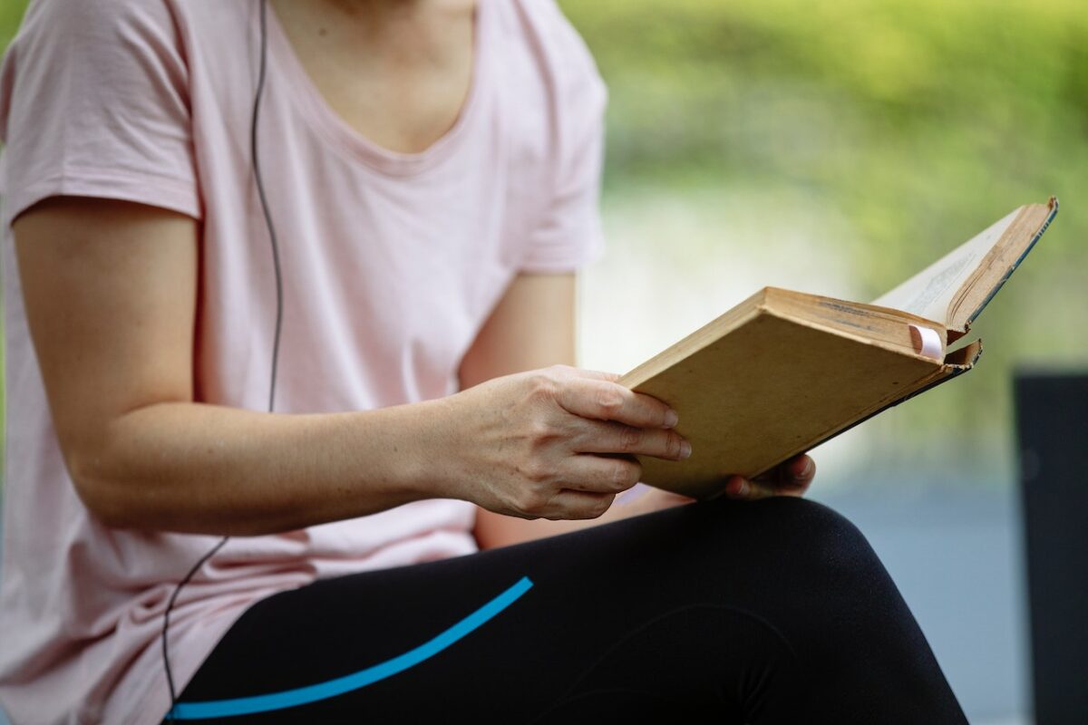 A person wearing a pink t-shirt and black leggings reading a book in the park