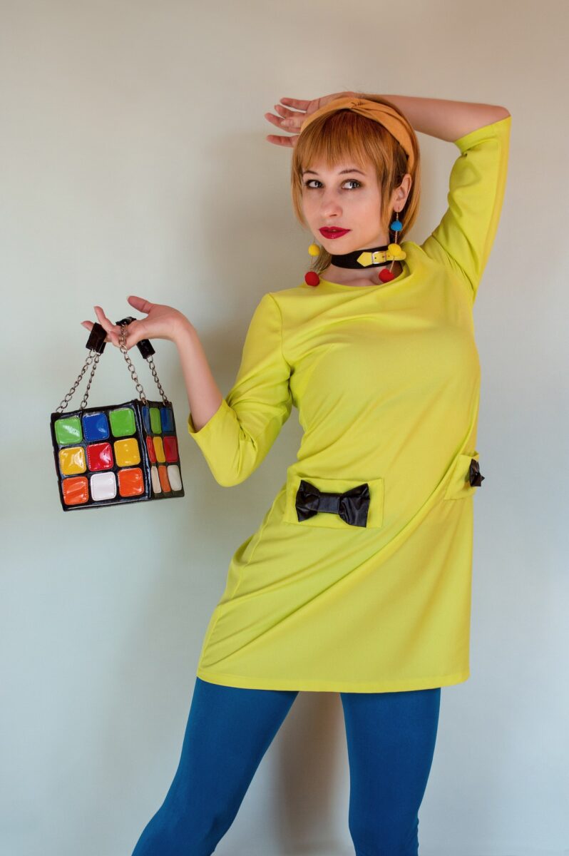 Woman in a yellow blouse and blue leggings holding a colorful bag