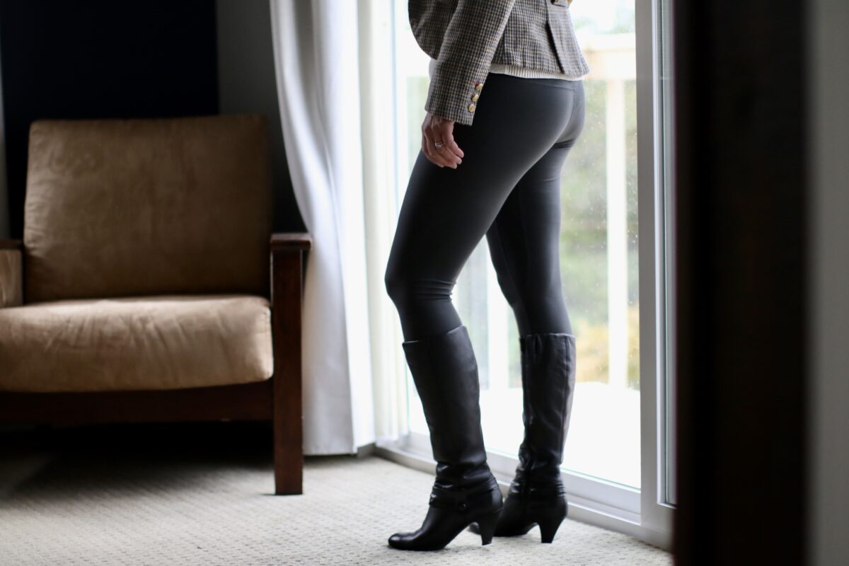 A person wearing black leggings and black high heel boots is standing on a gray carpet