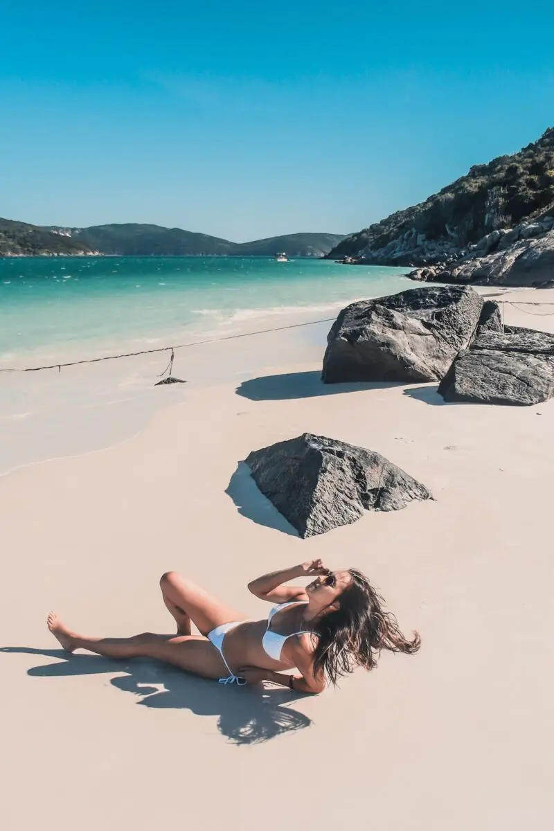 Woman in a white bikini wearing sunglasses lying on the shore of the beach