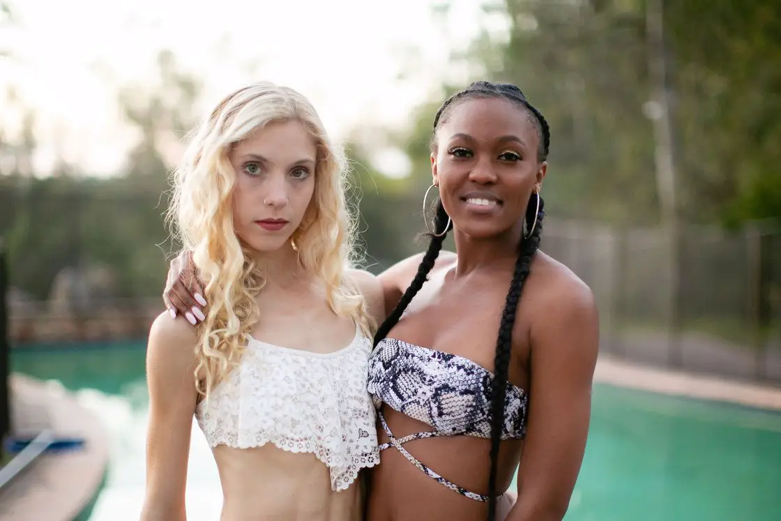 Two women posing together near a pool while wearing different types of bikins