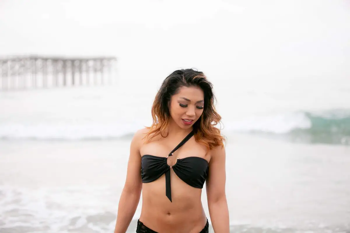 A woman wearing a black one-shoulder bikini top and underwear on the beach