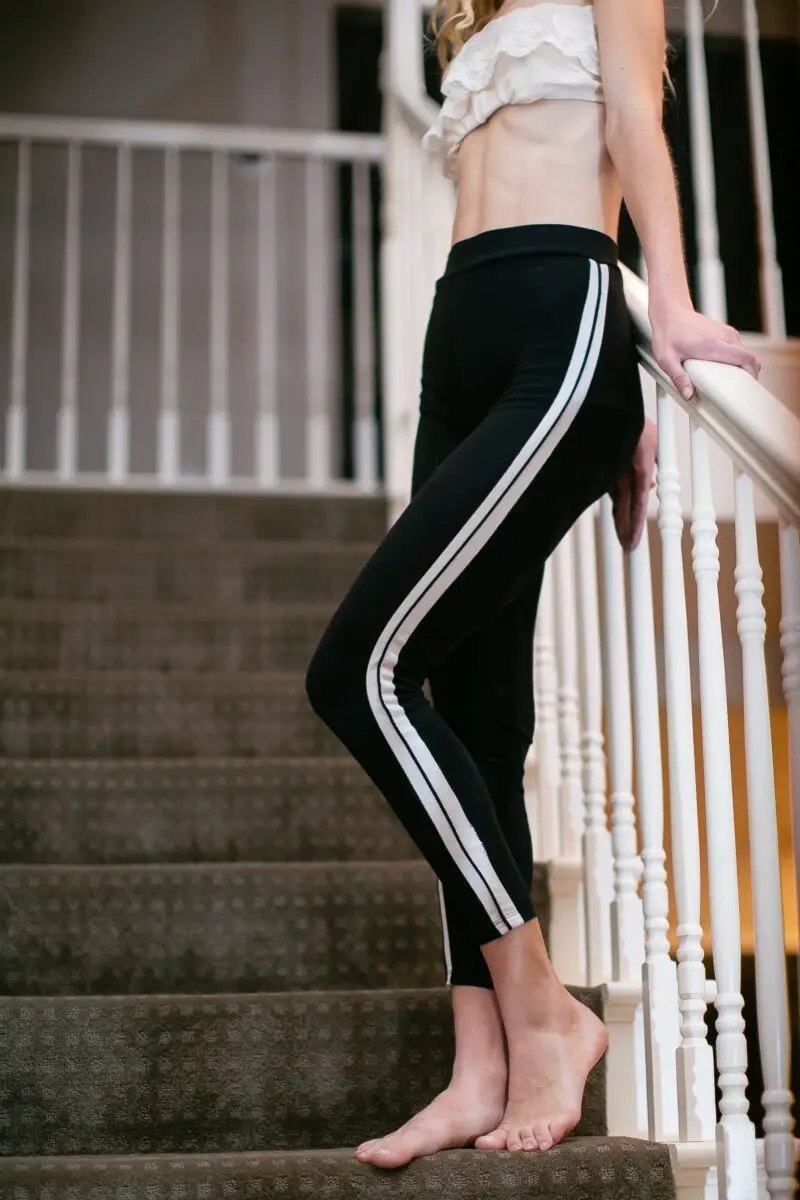 A woman wearing a crop top blouse and black leggings with white striped is standing on the stairs
