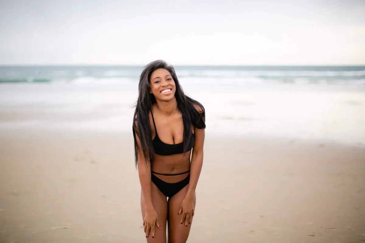 A woman wearing a black bikini stands in the sand
