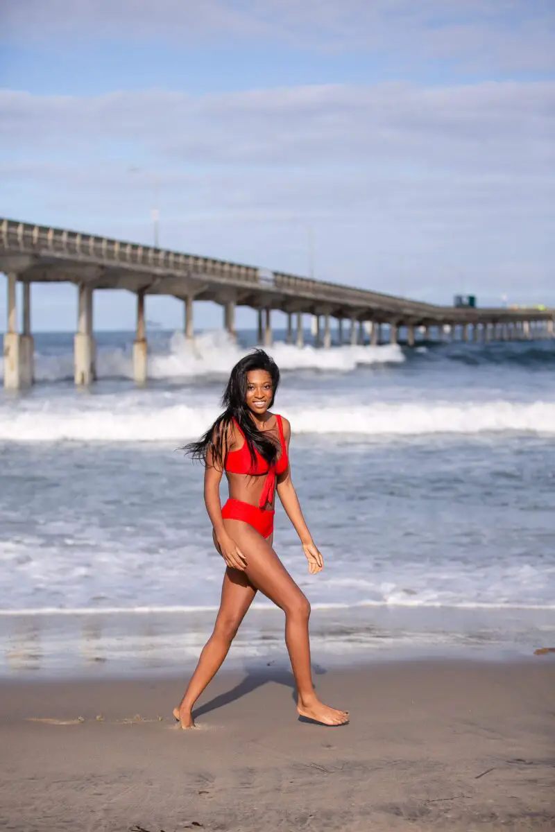 A woman walking in the sand while wearing a red bikini