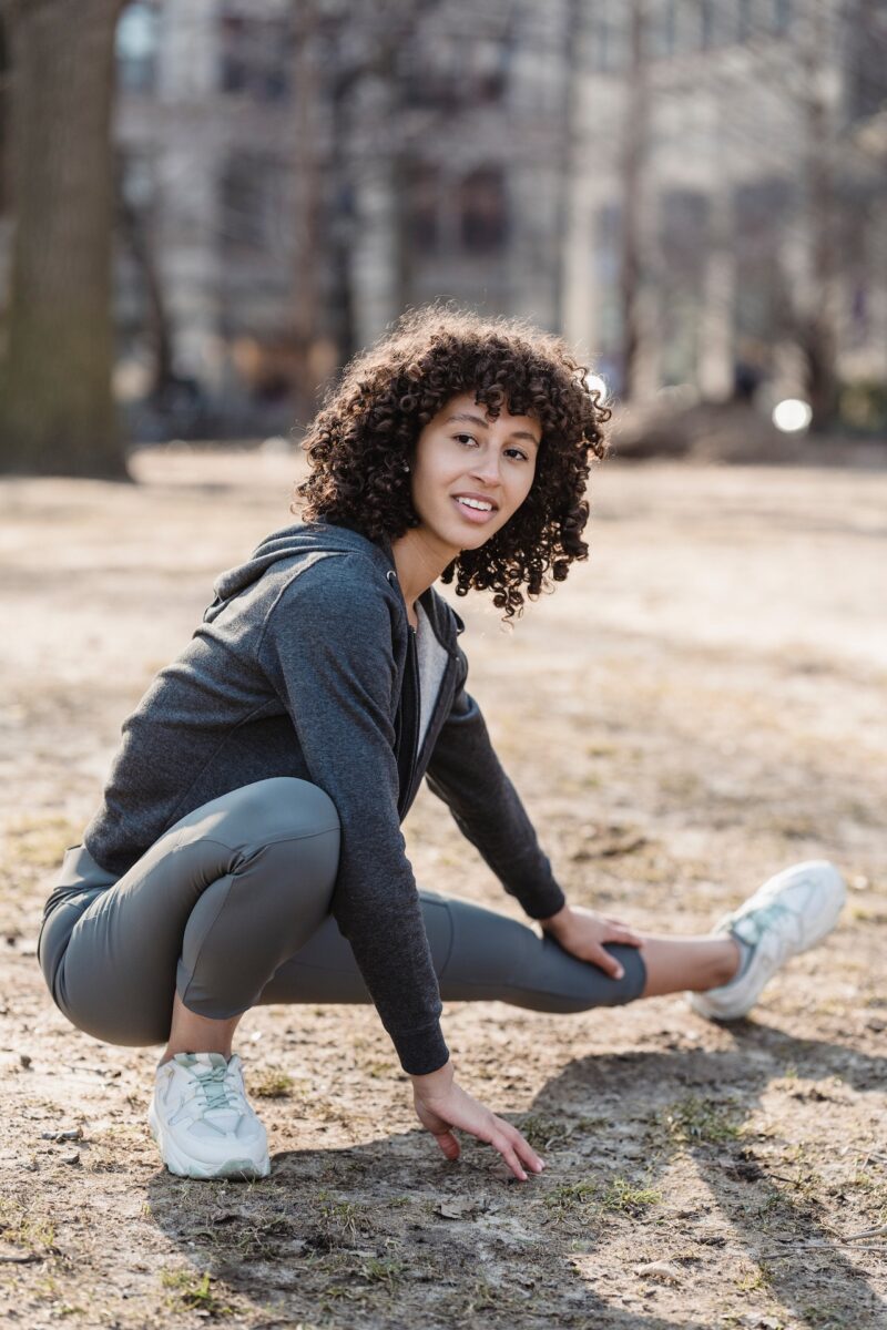 A woman wearing a gray sweatshirt and gray leggings doing stretching in the park