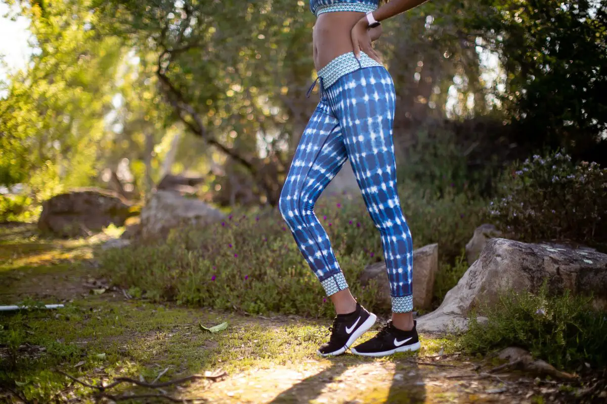A blue sports bra, leggings, and black rubber shoes are worn by a person in the park