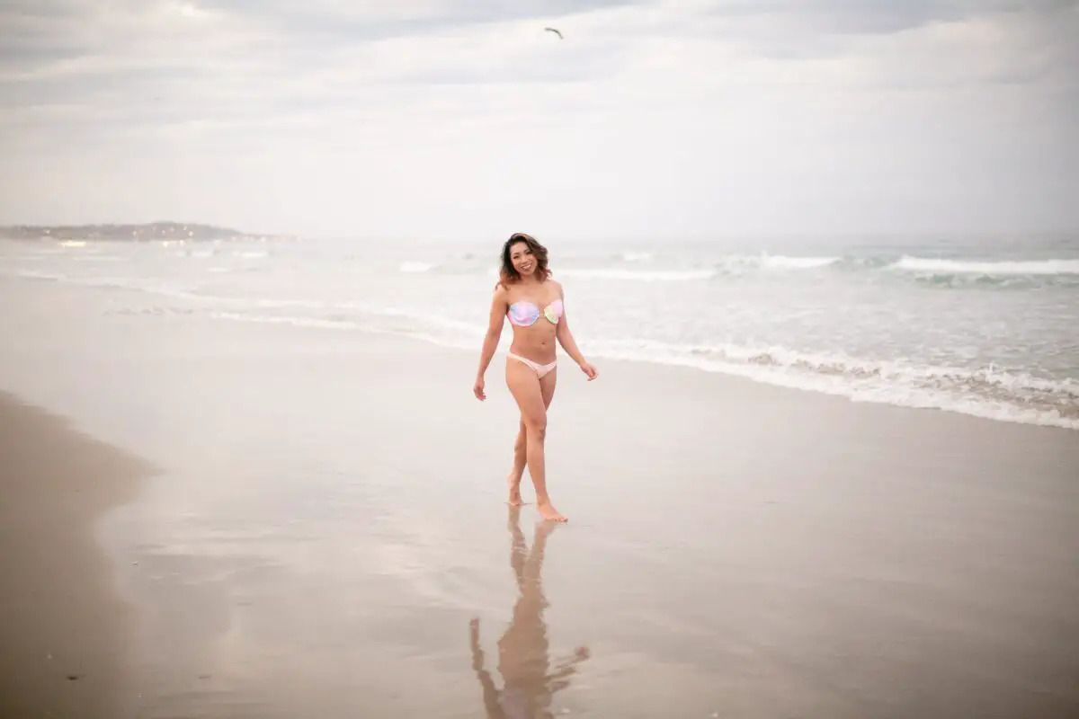 A woman wearing a light-colored bikini walks on the sand on the beach