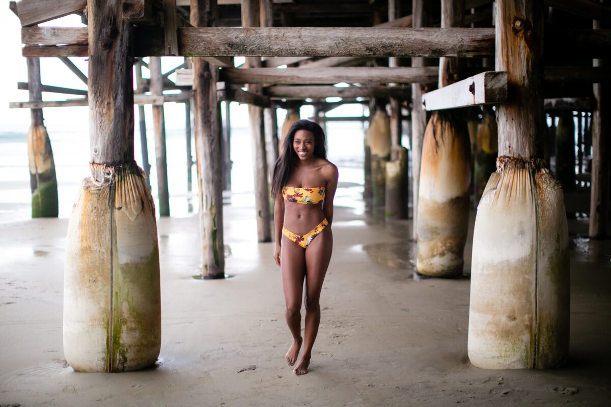 A woman wearing a yellow bikini with a floral design stands on the sand