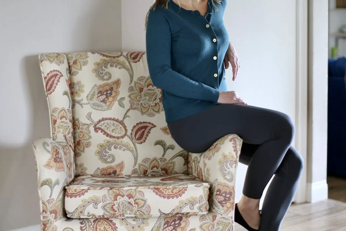 A woman wearing blue long sleeves and gray leggings is seated on a sofa