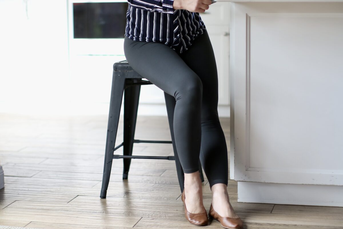 A woman wearing long sleeves and black leggings seated on a black chair