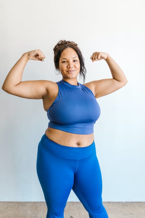 Woman wearing a blue cropped top and blue leggings while posing with her arms up