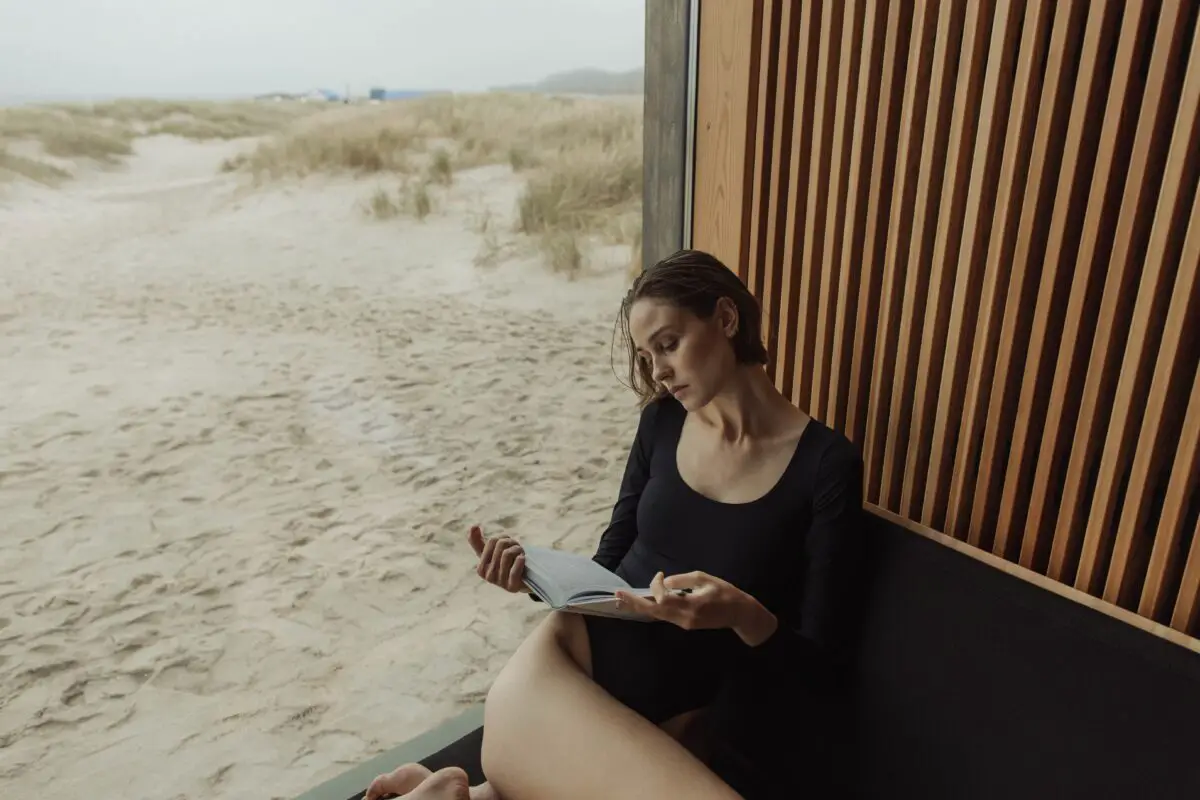A woman with black leotards reading in the entryway of a room near a beach