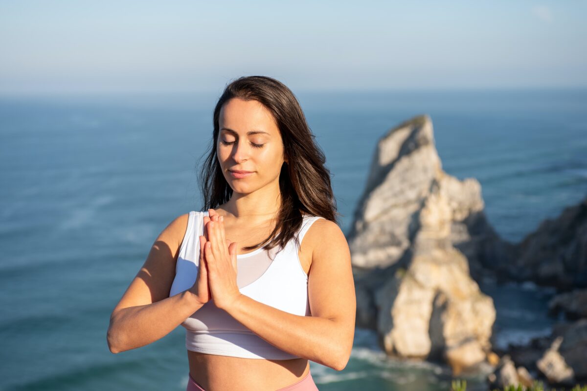 A woman meditating outdoor wearing a white sports bra
