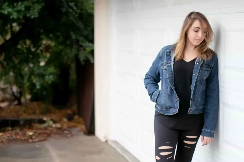 Woman wearing a blue jean jacket on top of a black shirt and ripped black leggings