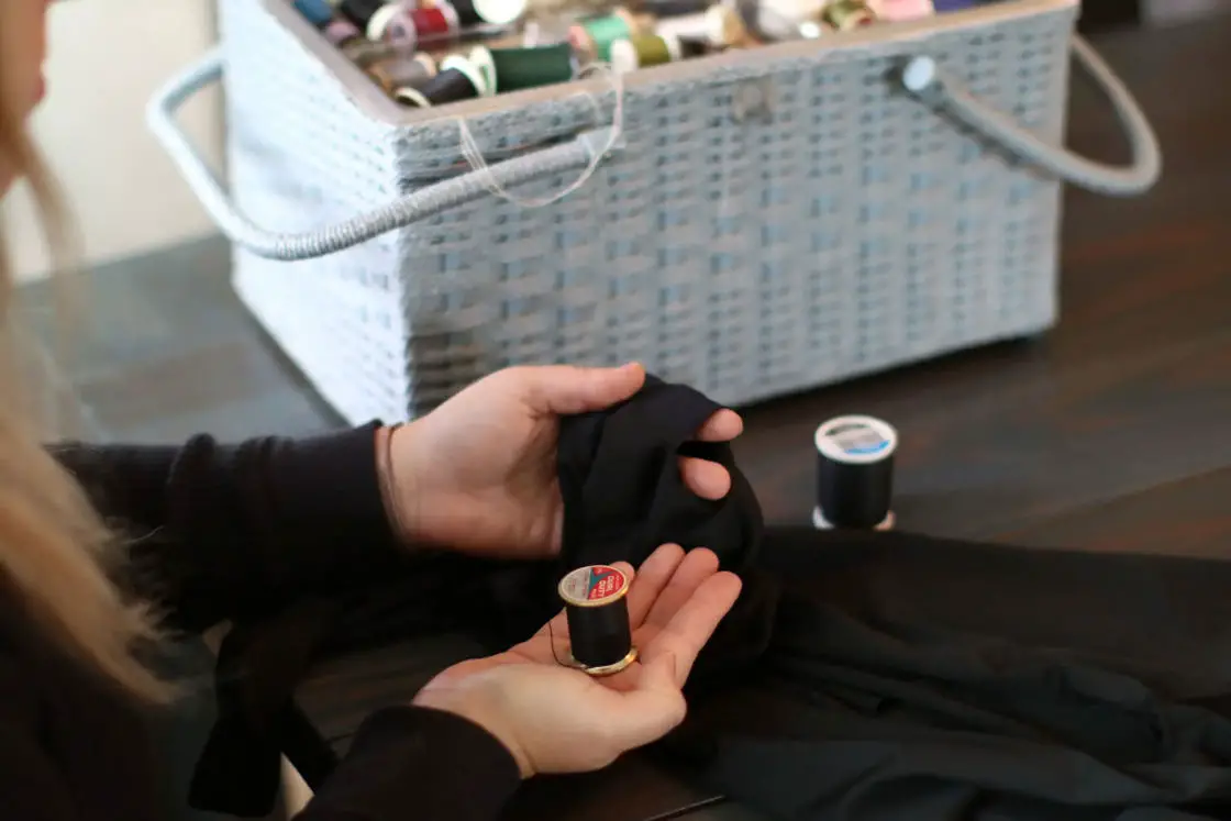 Woman holding a black thread spool while looking at her black leggings that was ripped