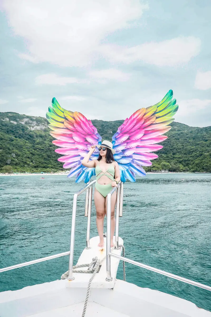 Woman wearing a green monokoni with rainbow colored wings while standing at the edge of a yacht