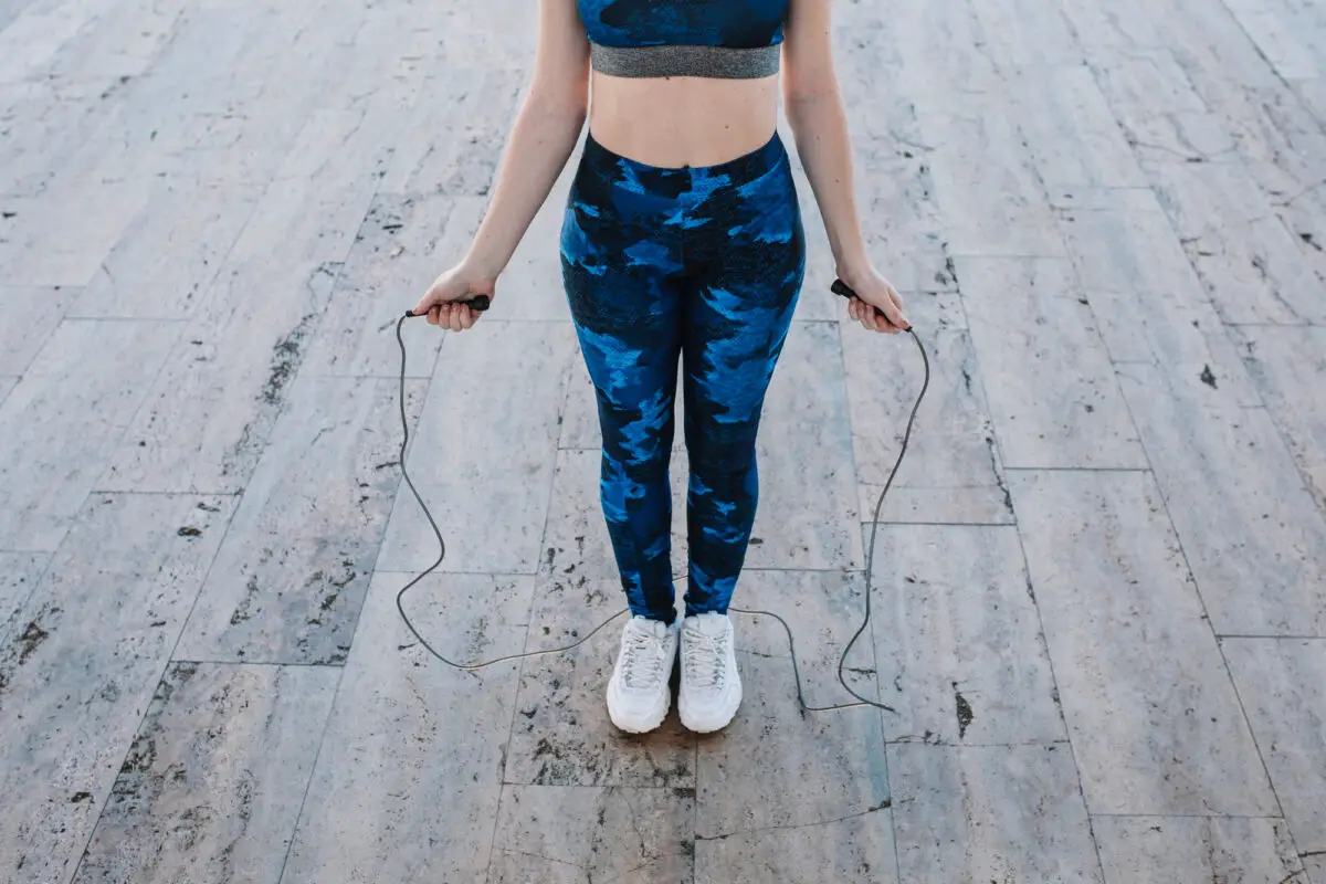 A woman wearing a blue camo leggings and sports bra holding a jumping rope